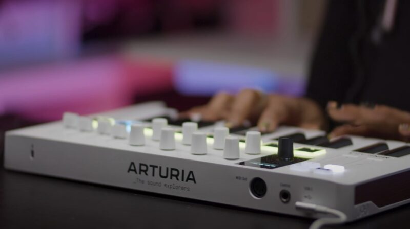 Hands expertly navigating the controls of a white Arturia synthesizer