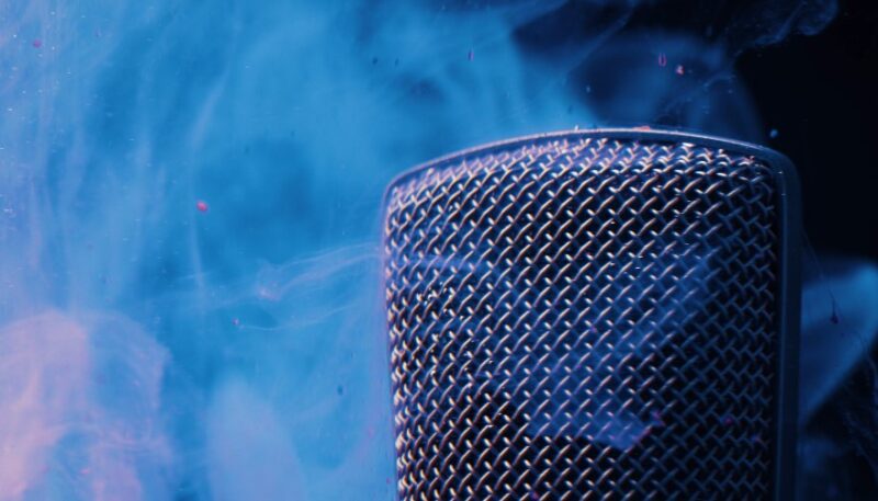 A close-up of a microphone, its metallic grill shimmering in the vibrant blue haze