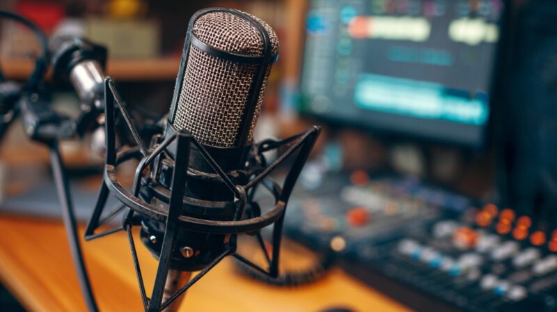 Close-up of a studio microphone with audio mixing equipment blurred in the background