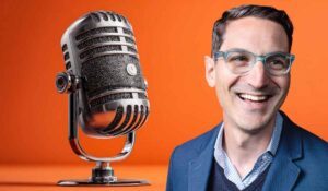 Smiling man beside a large vintage microphone on an orange background