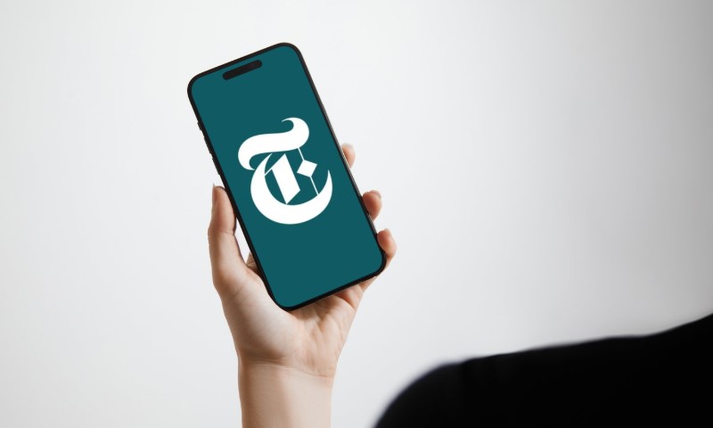 A person holding a phone with "NYT Audio" app opened
