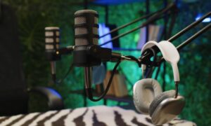 A podcast studio with two black microphones on adjustable arms and silver headphones placed on one